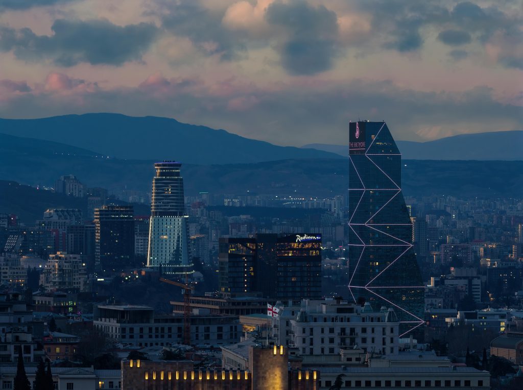A breathtaking aerial view of Tbilisi's skyline at twilight with illuminated buildings and distant mountains.
